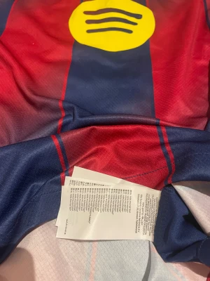 FC Barcelona Lamine Yamal tröja Nike S - Säljer en FC Barcelona matchtröja med Lamine Yamal och nummer 10 på ryggen. Tröjan är kortärmad, har klassiska blå och röda ränder, gula detaljer och sponsorloggor från Spotify och UNHCR. Tillverkad i lätt Dri-Fit polyester för maximal komfort. 