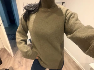 Olivgrön stickad polotröja - Snygg olivgrön stickad polotröja med hög krage och ribbade muddar vid ärmslut och nederkant. Perfekt för dig som gillar enkel och stilren design med lite edge på kragen. Passar dig som vill ha en varm och skön tröja till kyliga dagar.