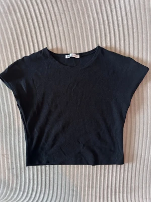 Svart croppad topp från Zara - Svart croppad topp från Zara med rund hals och korta ärmar. Enkel och stilren design i mjuk bomull som passar perfekt till jeans eller kjol. Toppen har en loose passform och är superbekväm för chill dagar. Snygg att styla med lager på lager.