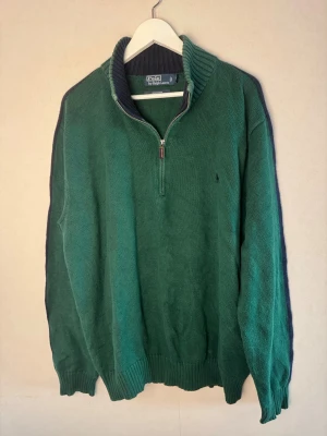 🔥Grön stickad tröja - Polo Ralph Lauren - 🔥Grön stickad tröja från Polo Ralph Lauren i storlek XXL. Tröjan har en ribbad krage i mörkblått, half zip-dragkedja med läderdetalj och långärmade muddar. Diskret logga broderad på bröstet. Perfekt för dig som gillar klassisk stil med en chill vibe. Liten fläck på vänster under ärm (kolla 4 bilden) men annars i ett mycket bra skick!