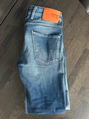 Replay jeans  - Säljer ett par ljusblå jeans från Replay med och slitning på höger knä. Jeansen har raka ben och snygga detaljer på bakfickorna. Perfekta för dig som gillar en avslappnad men trendig look.                                                       -Modellen är 184cm                                                -Nypris ca 1400kr