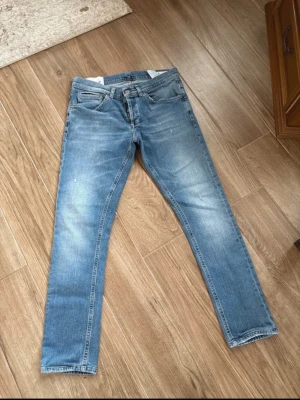 Dondup George skinny fit strl 32 - Snygga ljusblå jeans från Dondup i klassisk femficksmodell med orangea sömmar och Dondup märke på bakfickan. Jeansen har rak passform och är tillverkade i mjukt denimtyg som ger en skön känsla. Perfekt för dig som gillar stilrena och tidlösa jeans.