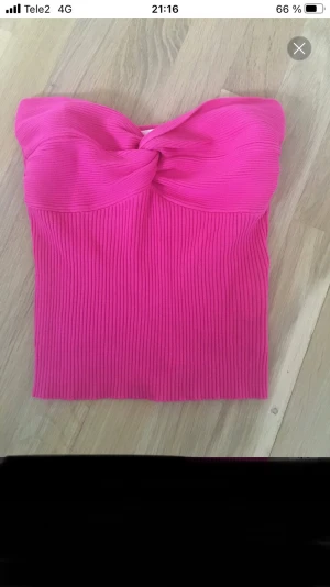 Ribbad rosa bandeau tubtopp - Säljer en snygg bandeau tubtopp i stark rosa färg. Toppen är ribbad och har en twistad detalj framtill som ger en cool look. Den är axelbandslös och har en tight passform som sitter perfekt. Perfekt för sommarens alla tillfällen!