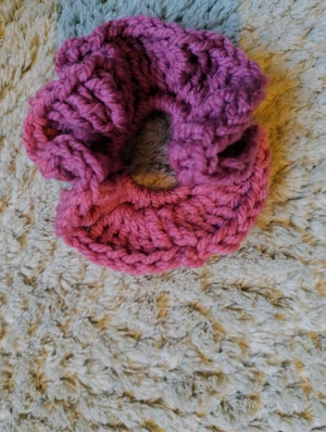 Handgjord rosa-lila virkad scrunchie - Superfin handgjord scrunchie i rosa. Perfekt för att ge din frisyr en färgklick och en mysig vibe. Den är fluffig och har en snygg volangkant som gör den extra söt. Passar både till uppsatt hår och som accessoar på handleden. Virkad av mig!