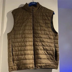 Brun quiltad dunväst från Zara - Quiltad brun dunväst från Zara i storlek L. Västen har hög krage, dragkedja framtill och två sidofickor. Perfekt för lager-på-lager och enkel att matcha med olika outfits. Snygg och funktionell för kyligare dagar.