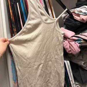 Beige ribbad linnetopp S/M - Säljer en ljusbeige ribbad linnetopp i storlek S/M. Toppen har smala axelband och är tillverkad i mjuk viskos med lite stretch från elastan. Perfekt för dig som gillar enkla och stilrena plagg med skön passform.