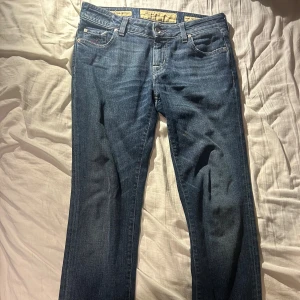 Jacob Cohen blå jeans med lila detaljer - Snygga blå jeans från Jacob Cohen med lila broderade detaljer och lila pälsmärke bak. Klassisk femficksmodell med raka ben och kontrastsömmar. Jeansen har metallknappar med logga och en liten broderad J på myntfickan. Perfekt för dig som gillar exklusiva jeans.