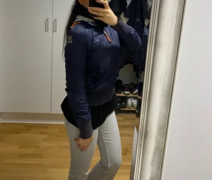 Mörkblå vindjacka från Parajumpers - Säljer en mörkblå vindjacka från Parajumpers med orange detaljer på dragkedja och huva. Jackan har ribbade muddar, huva med grå insida och snygg logga på ärmen. Perfekt för dig som gillar sportig och clean stil.