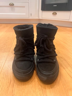 Svarta boots från Inuikii med snörning - Säljer ett par svarta vinterskor från Inuikii. Skorna har en platt sula och är fodrade med mjukt material för extra värme. Utsidan är i äkta mocka och skinn, vilket ger en snygg och lyxig känsla. Perfekta för kalla dagar och har en cool, chunky look. Även impregnerade och endast använd ca 5 gånger då de är lite för stora💗