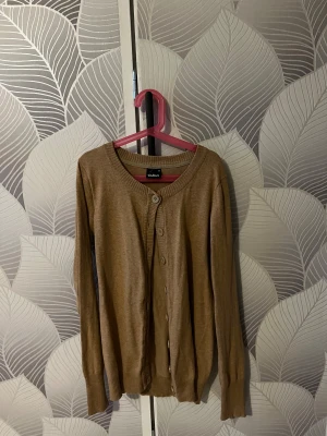 Beige kofta från Cubus  - Snygg beige kofta från Cubus i storlek M. Koftan har rund hals, långa ärmar och stängs med matchande knappar framtill. Materialet är mjukt och lätt, perfekt för lager-på-lager. Ribbstickade muddar vid hals, ärmslut och nederkant. Skriv vid frågor.