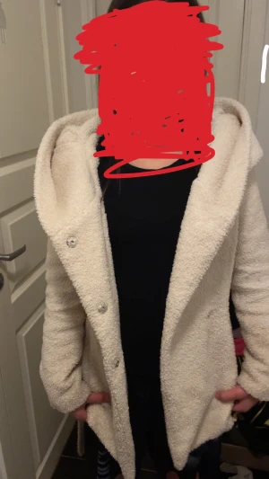 Vit teddyjacka med huva och bälte - Mysig vit teddyjacka med stor huva och bälte i midjan. Jackan har knappar framtill och är tillverkad i fluffigt teddy-material som ger en chill och trendig look. 