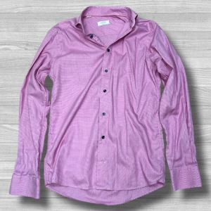 Rutig rosa skjorta från Eton slim fit - Snygg rosa skjorta från Eton i slim fit med diskret rutigt mönster. Skjortan har mörka knappar, klassisk krage och långa ärmar med manschett. Perfekt för dig som gillar stilrena detaljer och vill sticka ut med färg. Materialet är mjuk bomull som känns skönt mot huden.