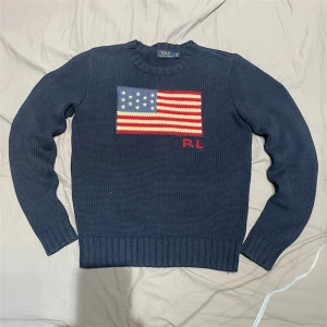 Mörkblå stickad flagg tröja Polo Ralph Lauren - Polo Ralph Lauren Flag Sweater – mörkblå stickad tröja med amerikansk flagga på bröstet och RL-broderi. Klassisk rund hals och ribbade muddar. Riktigt fin och fräsch, perfekt för dig som gillar tidlös preppy stil. Storlek S (passar XS–S). Skick 9/10 – inga fläckar eller hål. Nypris ca 3000-4000 kr. ✅ Äkta vara | 📩 Öppen för frågor | 🚚 Skickas inom 24 timmar 
