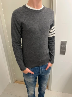 Grå stickad tröja Thom Browne - Stickad Thom Browne merino-ull tröja i size 3 - M. Men sitter som S. Kille i bild är 180, men det är för kort. Passar bäst 170-180. Skick 9/10. 