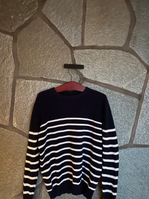 Mörkblå randig stickad tröja - Snygg mörkblå stickad tröja med vita horisontella ränder över bröstet och ärmarna. Tröjan har rund hals och långa ärmar, perfekt för dig som gillar klassisk och enkel stil..