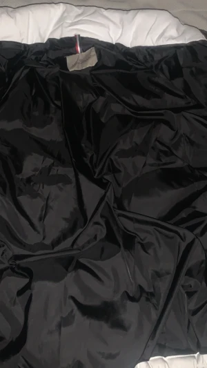 Vit Moncler pufferjacka med dragkedja - Säljer en snygg vit pufferjacka från Moncler med svart innerfoder och coola detaljer som Moncler-logga på ärmen. Jackan har hög krage, dragkedja och snörning nertill. Perfekt för dig som vill ha en stilren och varm jacka med exklusiv känsla.