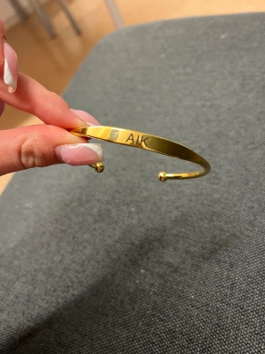 Guldigt AIK-armband - Snyggt och stilrent armband med ”AIK” gravyr på  i guld. Armbandet är i rostfritt stål och är i mycket bra skick💛🖤