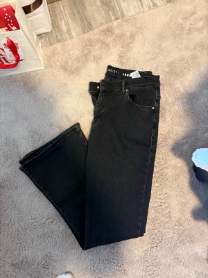 Svarta raka jeans - Säljer ett par svarta lågmidjade bootcut jeans med klassisk femficksdesign. Jeansen har normal midja och är tillverkade i ett mjukt denimtyg som känns skönt hela dagen. Perfekta för dig som gillar en enkel och stilren look.