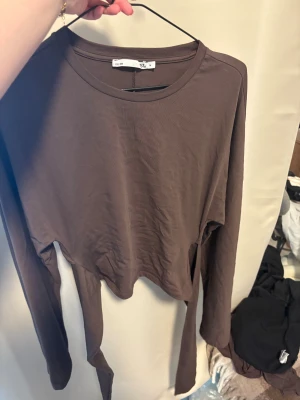 Brun långärmad topp  - Säljer en brun långärmad topp från Lager 157 med rund hals och coola långa knytband baktill. Toppen har en tajt passform och är tillverkad i mjuk bomull, perfekt för dig som gillar chill och stilren vibe.