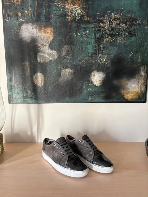 Bruna mockasneakers från Lanvin - Snygga sneakers från Lanvin i brun mocka med svarta lackdetaljer på tån och vita sulor. Skorna har klassisk snörning och rund tå, vilket ger en clean och stilren look. Perfekta för dig som gillar exklusiva och tidlösa sneakers med en twist.