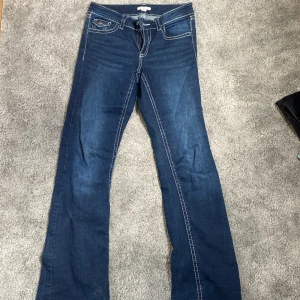 Blå bootcut jeans från Gina Tricot - Mörkblå jeans från Gina Tricot med bootcut passform och kontrastsömmar. Klassiska femficksdetaljer och snygga bakfickor med lock och knapp. Tillverkade i jeansmaterial, perfekta för en trendig och avslappnad look.