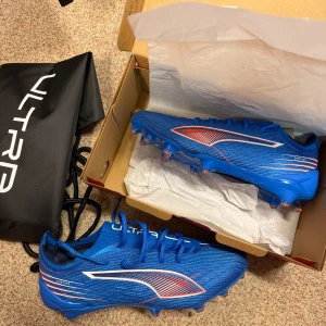 Blåa Puma Ultra fotbollsskor - Säljer ett par grymma blåa Puma Ultra fotbollsskor med snygga röda och vita detaljer. Skorna har snörning, låg profil och är tillverkade i lätt syntetmaterial för maxad speed på planen. Perfekta för dig som vill sticka ut och dominera matchen. Storlek 40 men skulle säga att de passar som 40,5-41