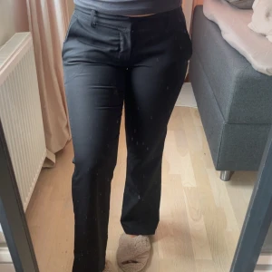 Svarta kostymbyxor med bootcut - Snygga svarta kostymbyxor med bootcut och normal passform. Byxorna har hällor för bälte, fickor fram och dekorativa fickor bak. Perfekta för en clean och stilren look. Materialet är slätt och känns bekvämt mot huden.