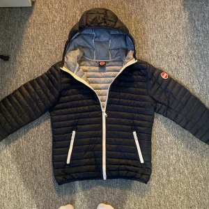  pufferjacka från Colmar - Säljer en pufferjacka från Colmar med huva och vita dragkedjor. Jackan har quiltad design, två fickor med dragkedja och en snygg logga på ärmen. Perfekt för kyliga dagar och riktigt skön att ha på sig.