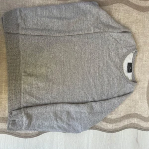 Grå crewneck sweatshirt från H&M - En stilren grå crewneck sweatshirt från H&M i regular fit. Tröjan har rund halsringning, ribbade muddar vid ärmslut och nederkant samt är tillverkad i en mjuk bomulls- och polyestermix. Perfekt för en chill och enkel look.