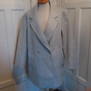 Ljusgrå kappa från 157, storlek M - Säljer en stilren ljusgrå kappa från 157 i storlek M. Jackan har klassisk krage, dubbelknäppning med knappar och två fickor framtill. Perfekt för dig som gillar enkel och clean stil. Materialet känns mjukt och passar bra till höst och vår. Aldrig använd