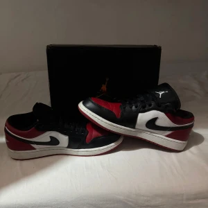 Nike Air Jordan 1 Low Gym Red/Black - Säljer ett par Nike Air Jordan 1 Low i färgerna gym red, svart och vitt. Klassisk siluett med svart swoosh, röd tåbox och vita paneler. Skorna har snörning, låg profil och ikonisk Jumpman-logga på plösen. Perfekta för dig som vill sticka ut med en tidlös sneaker.