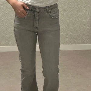 Grå bootcut jeans. - Snygga grå jeans med bootcut passform och hög midja. Jeansen har fem fickor, bälteshällor och råa, slitna kanter vid bensluten. Tillverkade i mjukt denimtyg som ger en bekväm känsla hela dagen.