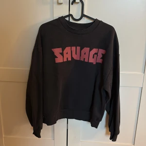 Svart sweatshirt med röd SAVAGE-tryck - Cool svart sweatshirt med stort rött SAVAGE-tryck på bröstet. Tröjan har rund halsringning, långa ärmar och en loose passform. 