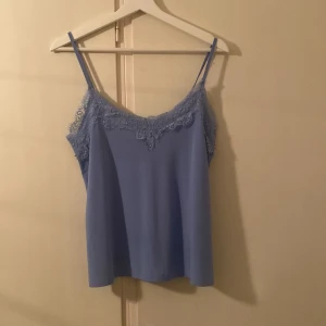 Ljusblå linnetopp med spets från Amisu - Supersöt ljusblå linnetopp från Amisu med tunna axelband och v-ringning dekorerad med spets. Toppen har en flowy passform och spetsdetaljer både fram och bak. Perfekt att styla med jeans eller kjol för en fräsch look.