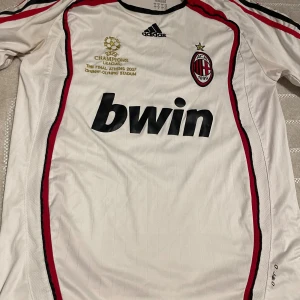 AC Milan  Champions League tröja - AC Milan fotbollströja från Adidas, Champions League-finalen 2007. Vit med röda och svarta detaljer, tryck med Beckham och nummer 7 på ryggen. Broderat klubbmärke och guldtext framtill. Tillverkad i polyester, klassisk passform och korta ärmar. 