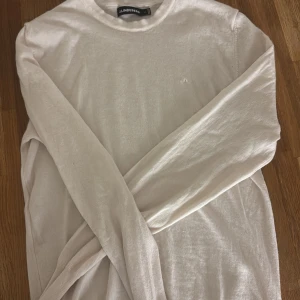 Beige långärmad tröja från J.Lindeberg - Snygg beige långärmad tröja från J.Lindeberg i mjukt material. Enkel och stilren design med rund halsringning och diskret logga på bröstet. Perfekt för dig som gillar minimalistisk och clean stil.