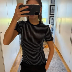 Blåtvit randig T-shirt med volangärm - Säljer en mörkblå topp med vita tunna ränder och volangdetaljer vid ärmslut och nederkant. 