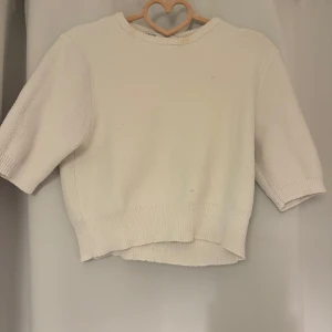 Vit stickad tröja från Zara - Superfin vit stickad tröja från Zara med kortare ärmar och rund hals. Tröjan har en mjuk och lite fluffig känsla, ribbade muddar och en något boxig passform. Perfekt att styla med jeans eller kjol för en clean look.