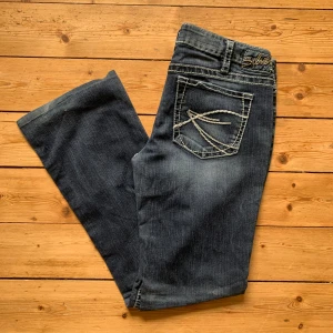 Silver Jeans Aiko bootcut jeans blå W34 L30 - Snygga blå bootcut jeans från Silver Jeans, modell Aiko. Jeansen har kontrastsömmar, klassiska fem fickor och dekorativa broderier på bakfickorna. Tillverkade i jeansmaterial med en något tvättad look och normal passform.     Storlek: W34 L30