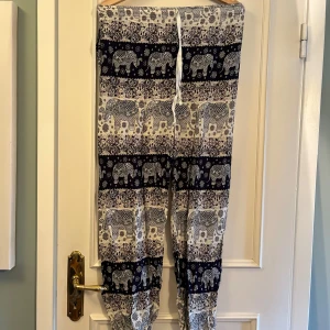 Mönstrade byxor med elefanter och snörning - Lätta och luftiga byxor med svartvitt elefantmönster och blommor. Byxorna har resår och snörning i midjan. Perfekta för chill dagar eller sommarhäng. Materialet känns som bomull.