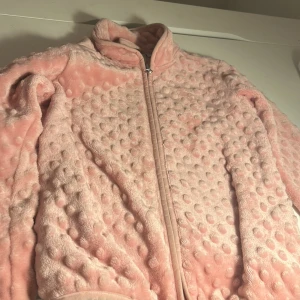 Rosa fleecejacka från Belle Amie - Supermjuk och fluffig rosa fleecejacka från Belle Amie med dragkedja framtill. Jackan har ett bubbligt, prickigt mönster i tyget och hög krage. Perfekt för dig som gillar mysiga och coola plagg med unik textur.