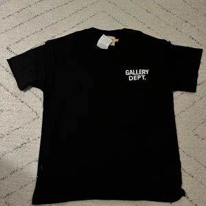 Svart Gallery Dept. t-shirt S - Svart t-shirt från Gallery Dept. med vit tryckt logga fram och stor text på ryggen. Klassisk rund hals och korta ärmar. Materialet är mjuk bomull och passformen är normal. Perfekt för dig som gillar streetwear och tydliga prints. Storleken är S men oversized. Skulle rekommendera för M. Fraktar direkt vid köp!