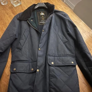 Mörkblå quiltad jacka Savvy Citizen - Quiltad mörkblå jacka från Savvy Citizen med klassisk krage i manchester,Perfekt för höst och vinter. Nypris: 3599kr