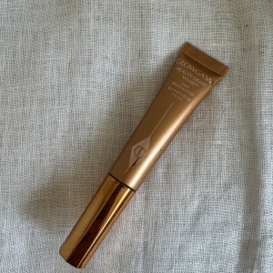 Charlotte Tilbury Glowgasm Highlighter Beauty Light Wand - Glowgasm Beauty Light Wand från Charlotte Tilbury i en lyxig guldbrun tub med applikator. Flytande highlighter som ger ett snyggt glow och är enkel att använda tack vare den mjuka svampapplikatorn. Perfekt för att framhäva kindben och ge ansiktet lyster.  Aldrig använd 