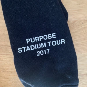 Svart Purpose Stadium Tour hoodie - Svart hoodie från Purpose Stadium Tour 2017 med röd TEAM-tryck på bröstet och turnéstäder på ryggen. Huva med snörning och känguruficka framtill. Mjuk bomullskänsla, perfekt för dig som gillar streetwear och vill sticka ut med tour-merch.