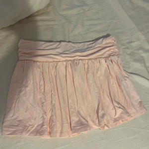 Ljusrosa kortkjol från Nelly - Supersöt ljusrosa kortkjol från Nelly med volangig och rynkad midja. Kjolen är i mjukt bomullstyg och har en flowy passform som ger en avslappnad och feminin look. Perfekt för dig som gillar en romantisk och trendig stil.