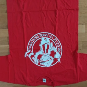 Ultras Atletico Madrid  - Röd långärmad tröja från Fruit of the Loom med stort vitt tryck framtill. Trycket visar en tecknad figur med bandana och texten 'Presos de un amor irracional'. Perfekt för dig som gillar unika statement-plagg.