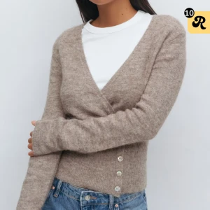 Beige omlottkofta med knappar - Supermjuk beige omlottkofta med v-ringning och tre snygga knappar framtill. Den är aldrig använd och har prislappen kvar!!! Koftan är långärmad och har en figurnära passform, perfekt att styla med jeans eller kjol. 