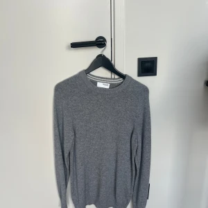 Grå stickad tröja från Selected Homme - En stilren grå stickad tröja från Selected Homme med rund halsringning och ribbade muddar. Perfekt för lager-på-lager och funkar lika bra till jeans som till chinos. Enkel och klassisk design som passar till det mesta. Storlek S passar M