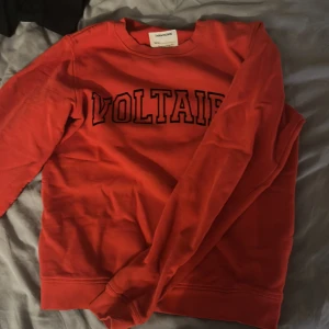 Röd sweatshirt från Zadig & Voltaire XS - Cool röd sweatshirt från Zadig & Voltaire i storlek XS. Tröjan har tryckt VOLTAIRE-text på bröstet och klassisk rund hals. Mjuk insida och ribbade muddar vid ärmslut och nederkant. Perfekt för en chill och avslappnad stil. Nypris 1200 säljer för 350 därmed hålet i tröjan 